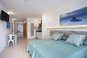 Un dormitorio con dos camas, un escritorio y una kitchenette.