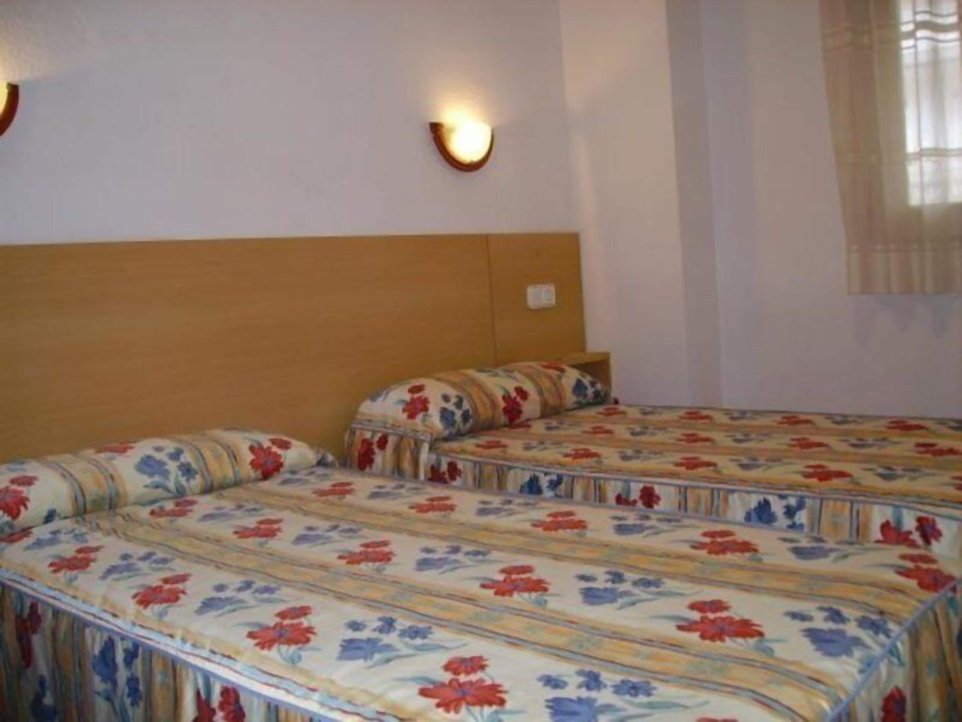 Une chambre dotée de deux lits, chacun agrémenté de draps à motifs floraux, de têtes de lit en bois et d’appliques murales.