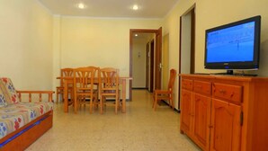 A living room with a sofa, wooden chairs, a dining table, and a TV on a wooden cabinet. - Rentalmar Bahia Dorada and Iris (Salou)