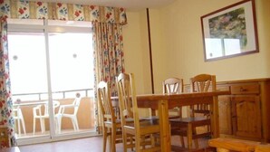 A dining area with wooden furniture, a balcony with white chairs, and a painting on the wall. - Rentalmar Bahia Dorada and Iris (Salou)