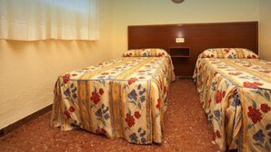 Una camera con due letti singoli, ognuno con copriletto a motivi floreali, una testiera in legno e un piccolo ripiano tra i letti.