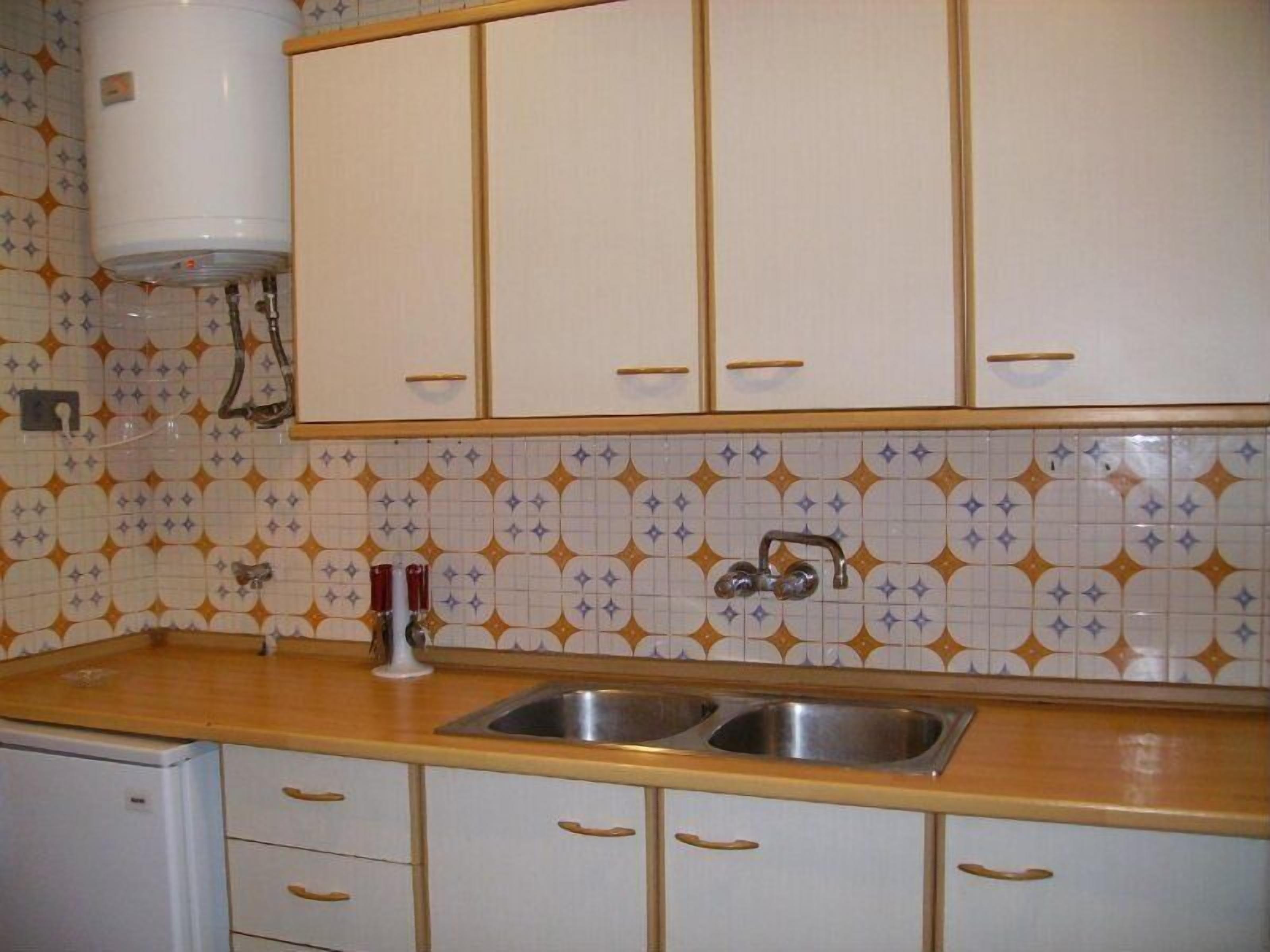 Cuina amb armaris blancs, vàscula d'acer inoxidable i enrere d'azulejos amb disseny.