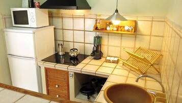 Cocina compacta con microondas, estufa, fregadero y un pequeño estante con utensilios de cocina.