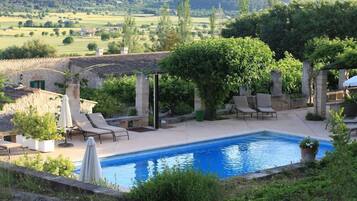 Zona de piscina con sillones de descanso, una pérgola y un edificio de piedra al fondo.