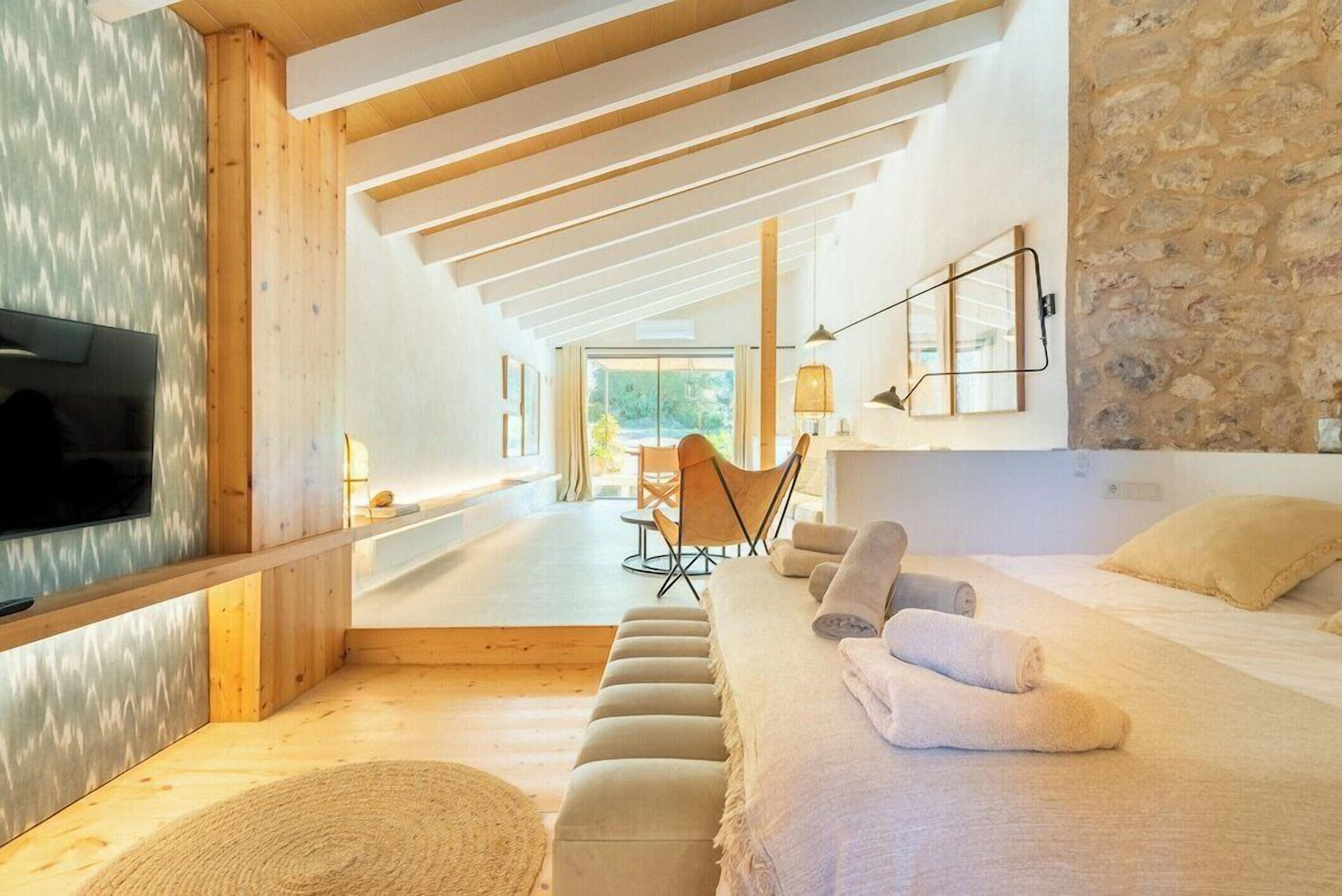 Una camera d'albergo moderna con soffitto in legno, un letto grande, una televisione e un muro in pietra.