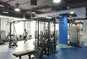 Ein Fitnessstudio mit unterschiedlichen Trainingsgeräten, einer Bank und einer Person, die geht.