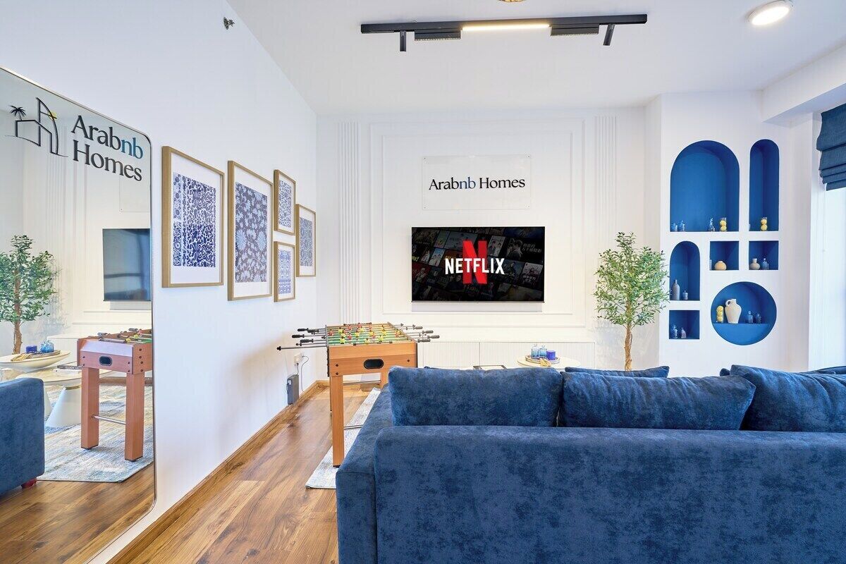 Un salon avec un canapé bleu, une table de baby-foot et un téléviseur fixé au mur qui affiche le logo de Netflix.
