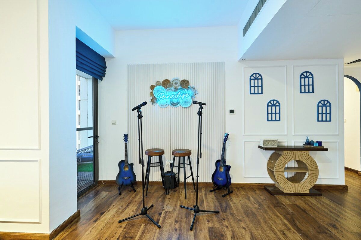 A room with a wooden floor, a neon sign reading 'Paradise,' and two guitars on stands.