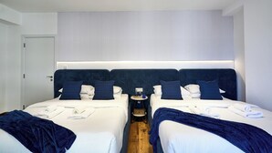Hotellihuone, jossa on kaksi sänkyä, yöpöytä lampun kanssa ja ikkuna, jossa on sälekaihtimet.