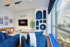 A modern living room with a foosball table, a TV displaying Netflix, and a view of a Ferris wheel through large windows. - Ocean Views / Karaoke / Foosball / Gym / Pool (Dubai)
