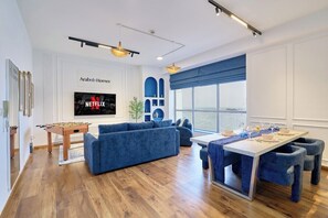 Un salon moderne avec un baby-foot, des canapés bleus, une table à manger avec des chaises bleues et une grande fenêtre donnant sur un beau paysage.