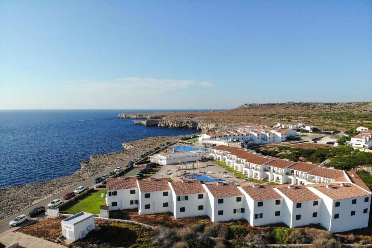 Un hôtel situé sur la côte, avec des bâtiments blancs, une piscine et une vue sur la mer.