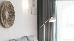 Een moderne slaapkamer met een grijze bank, gestreepte kussens, een wandkunst van geweven materiaal, een vloerlamp en een raam met gordijnen.