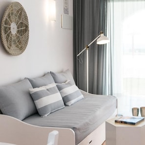 A modern bedroom with a grey sofa, striped pillows, a woven wall art piece, a floor lamp, and a window with curtains. - Menorca Sea Club (Ciutadella de Menorca)
