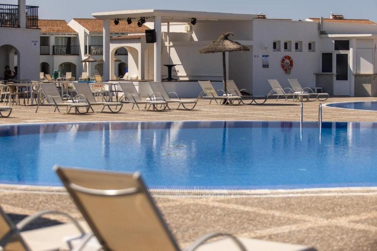 A pool area with lounge chairs and a building with a tiled roof.