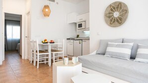 Een moderne, goed verlichte kamer met een eethoek, kitchenette en een bank met gestreepte kussens.