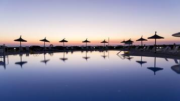 Ein Poolbereich mit Liegestühlen und Sonnenschirmen bei Sonnenuntergang.