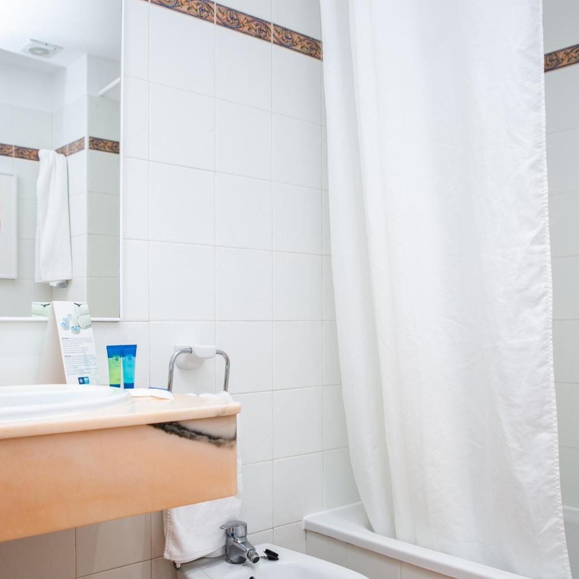 Un baño con lavamanos blanco, un espejo, toallero y cortina de ducha.