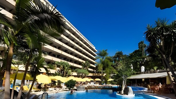 A hotel with a large pool, palm trees, and yellow umbrellas. - Fergus Puerto de la Cruz (Puerto de la Cruz)