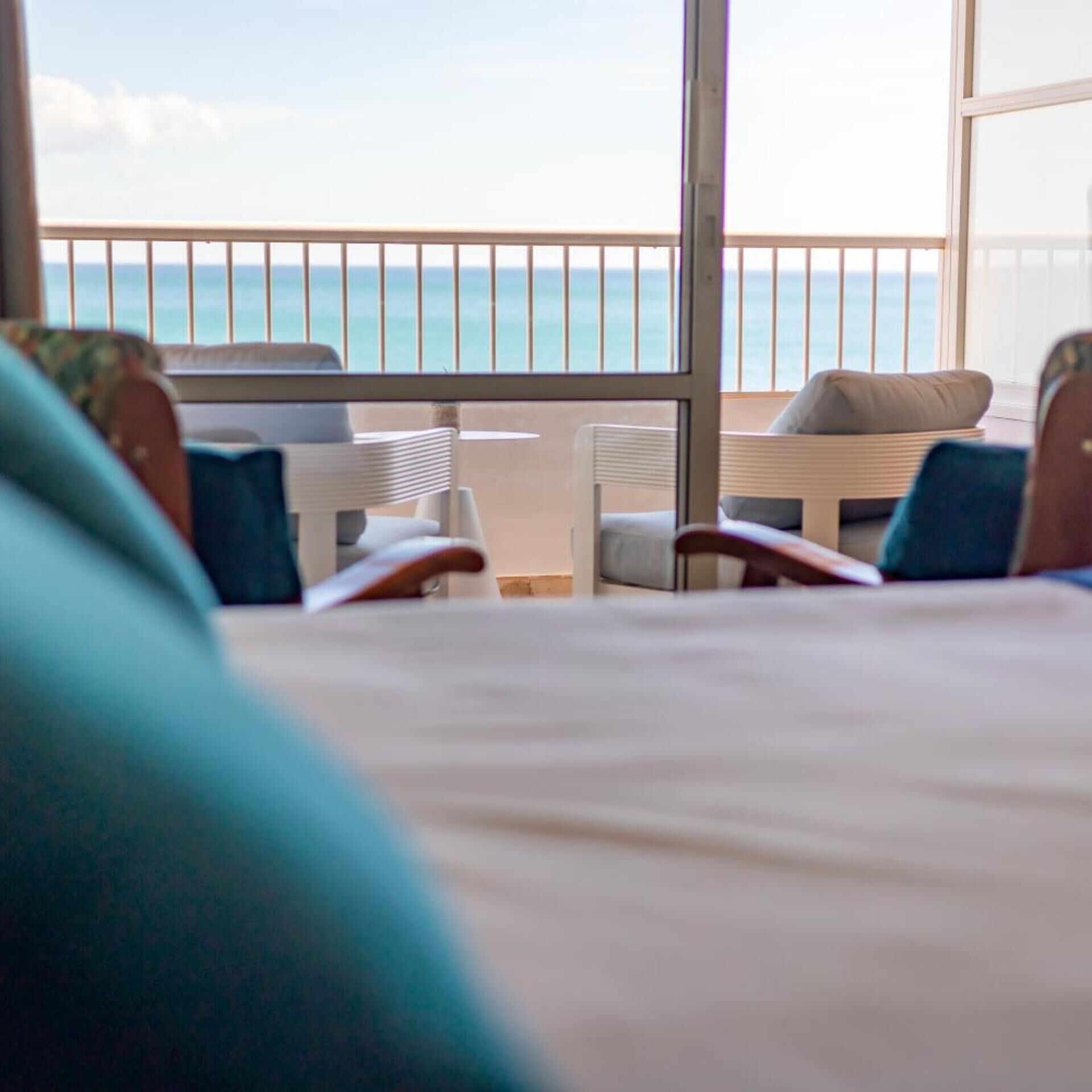 A hotel room with a balcony overlooking the sea, featuring a bed, two chairs, and a small table.