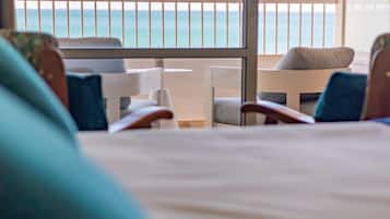 A hotel room with a balcony overlooking the sea, featuring a bed, two chairs, and a small table.