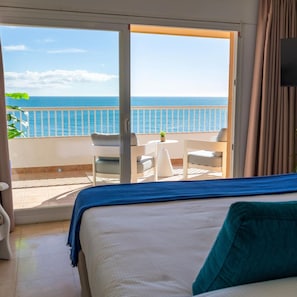 A hotel room with a bed, a small table, and a chair. The room has a view of the sea through a sliding glass door. - Apartamentos La Jabega (Fuengirola)