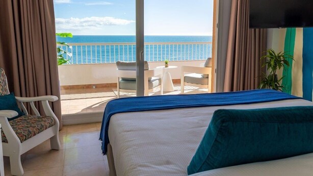Ein Hotelzimmer mit Bett, Sessel, kleinem Tisch und Meerblick.