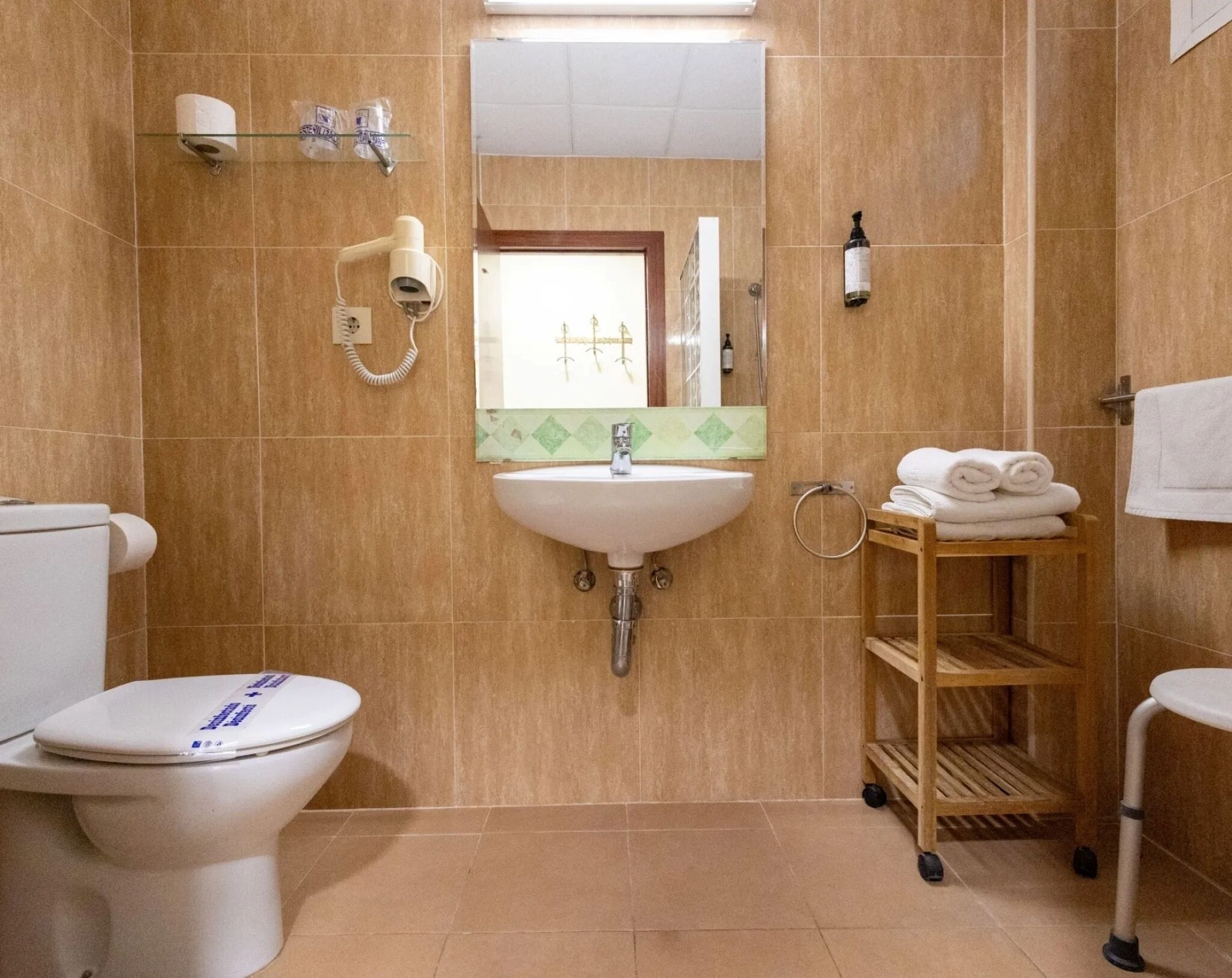 Et badeværelse med toilet, vask, spejl, håndklædestang og en hylde med håndklæder.