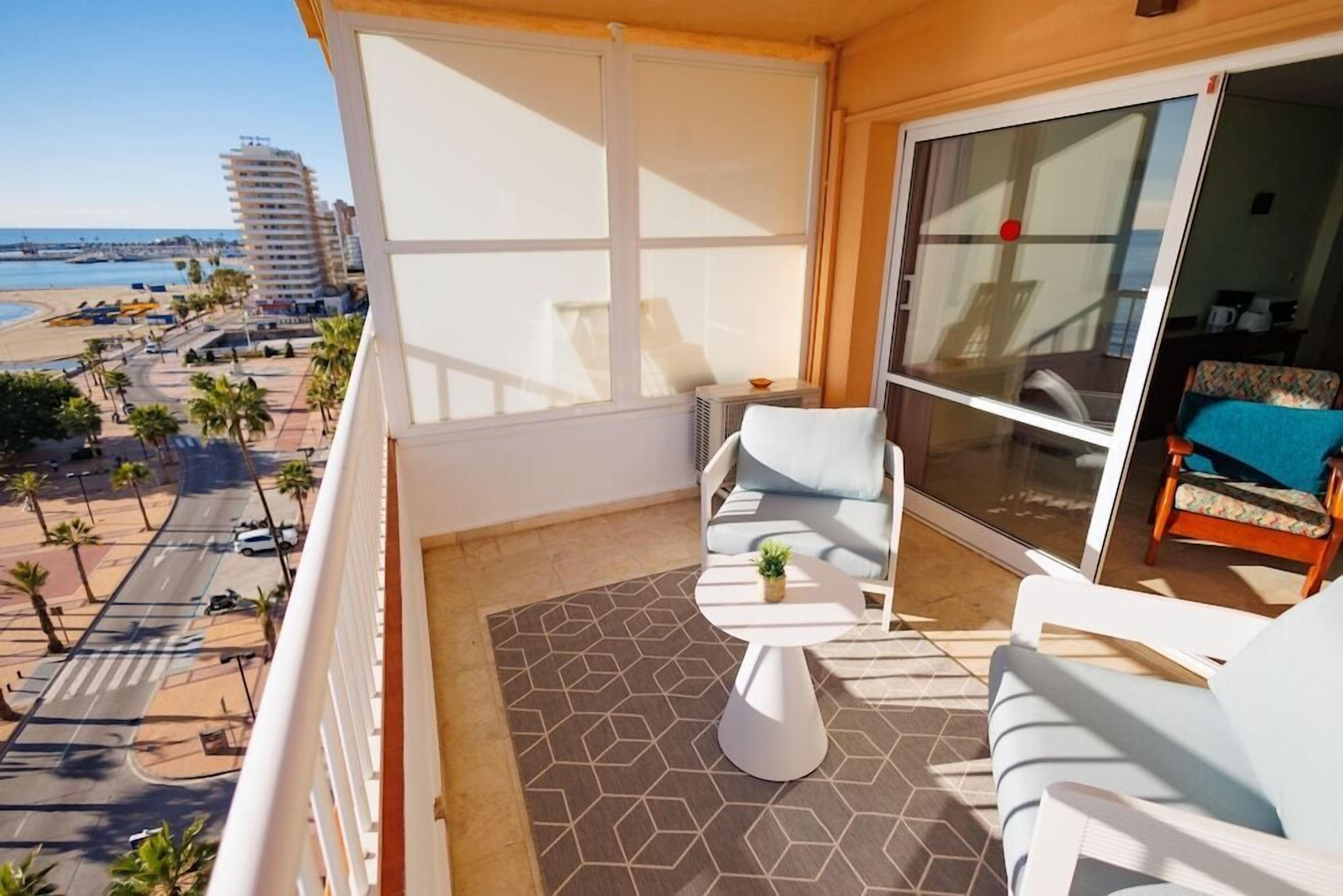 Un balcon avec vue sur la plage, une chaise blanche, une petite table et un canapé.