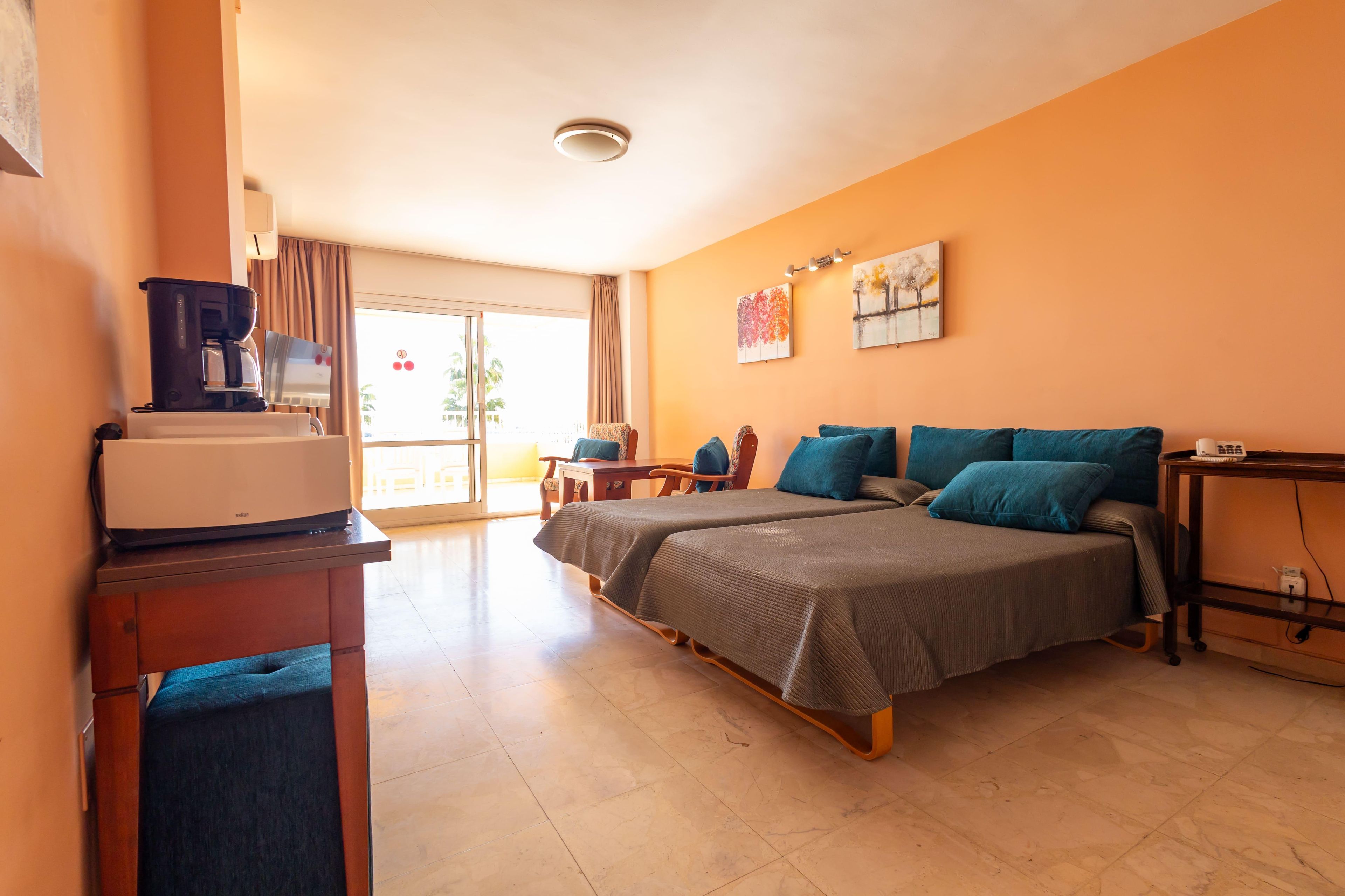 A hotel room with a bed, a desk with a coffee maker, a telephone, and a painting on the wall.