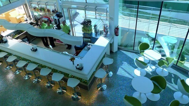 A modern bar area with a curved counter, bar stools, and a view of the outdoors through large windows. - Riviera Beach Hotel - Adults Only (Benidorm)