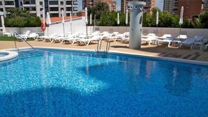 A swimming pool with sun loungers and umbrellas, surrounded by buildings and greenery. - Riviera Beach Hotel - Adults Only (Benidorm)