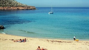 A beach with clear blue water, a sailboat, and people sunbathing. - Aparthotel Nereida (Sant Josep de sa Talaia)