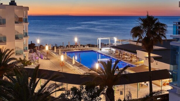 A pool area with a sunset view, lounge chairs, and a palm tree. - Aparthotel Nereida (Sant Josep de sa Talaia)