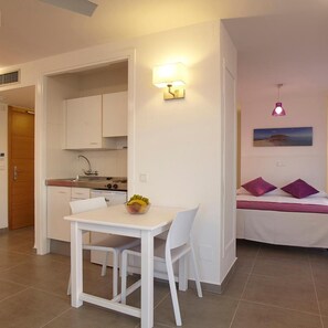 A compact living space with a kitchenette, dining area, and a bed with pillows. - Aparthotel Nereida (Sant Josep de sa Talaia)