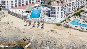 A coastal hotel with multiple balconies, a central swimming pool, and a rocky shoreline. - Aparthotel Nereida (Sant Josep de sa Talaia)