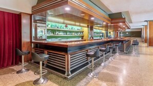 Una zona de bar con una barra alargada, varios taburetes y una estantería bien surtida con botellas.