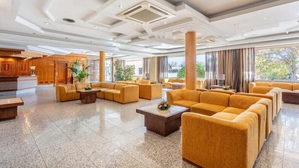 Un lobby espacioso con diseño moderno, que cuenta con una zona de estar central con sofás y una mesa de centro, rodeada de grandes ventanales con vistas al exterior.