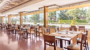 Un comedor amplio con varias mesas y sillas, ventanas grandes que ofrecen vistas al exterior y un diseño de techo moderno.
