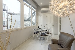 A dining area with a table set for four, white chairs, and a view of a building with a staircase. - Marques DE Pombal Vintage by Homing (Lisbon)
