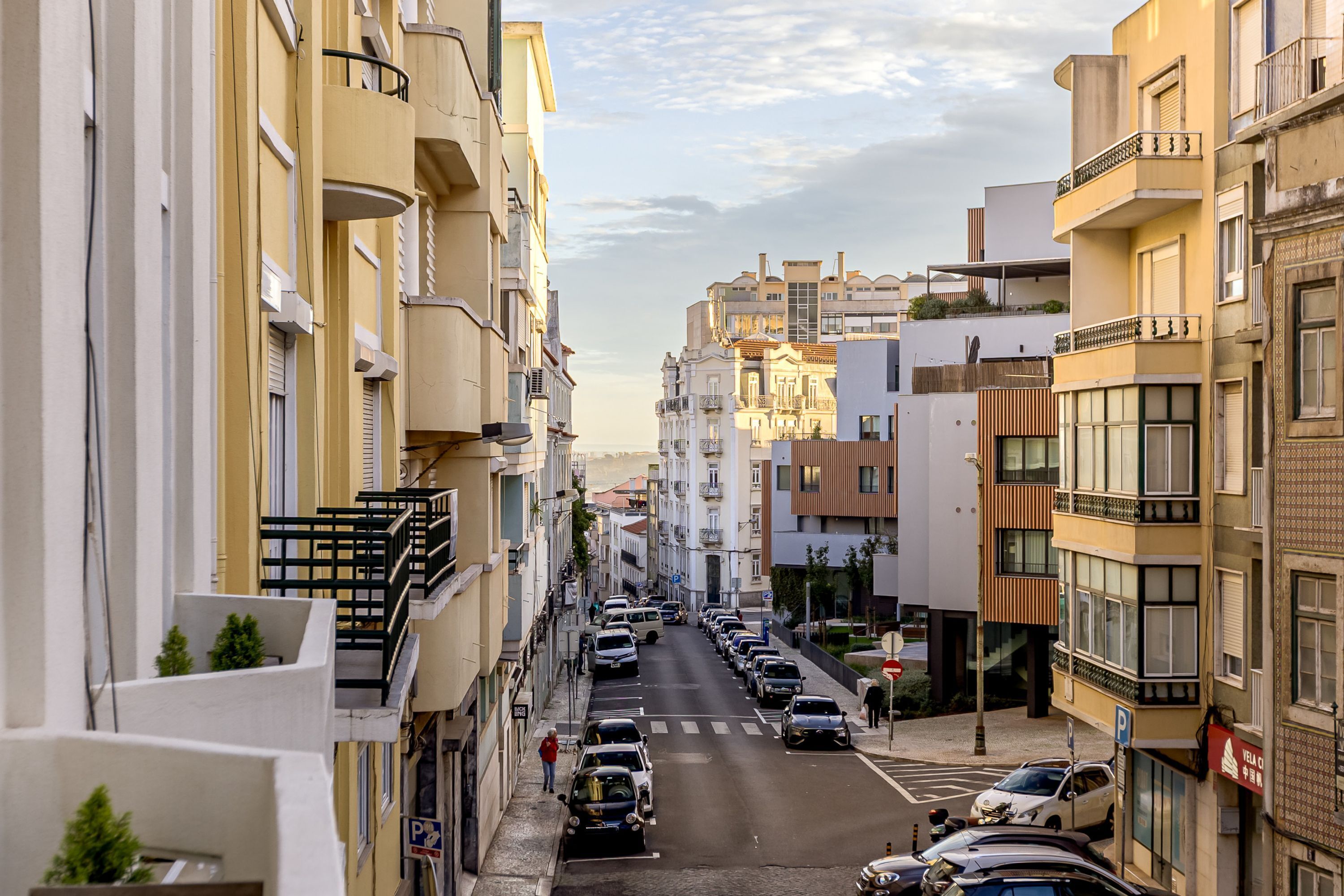 A street view with multi-story buildings, parked cars, and a pedestrian.