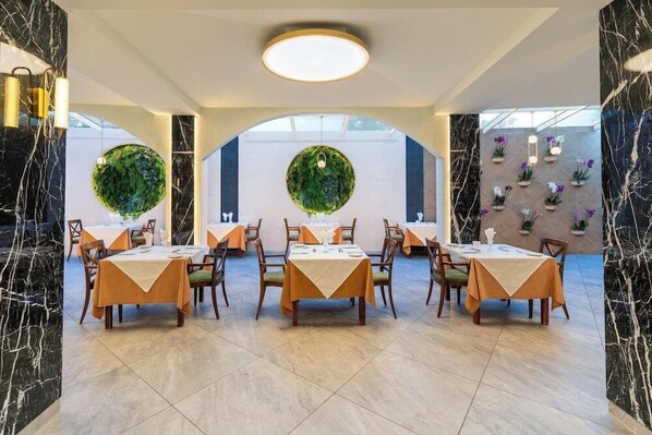 Restaurante com paredes de mármore, decorações redondas verdes na parede e mesas dispostas com toalhas laranja.