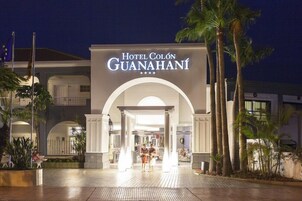 Hotel Colón Guanahani's entrance with a large arched doorway, palm trees, and a well-lit facade.