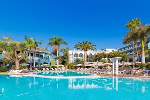 A hotel pool area with lounge chairs, palm trees, and a clear blue sky.
