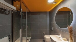 Ein modernes Badezimmer mit dunklen Fliesen, einer begehbaren Glasdusche, einer Toilette und einem Waschbecken mit rundem Spiegel.