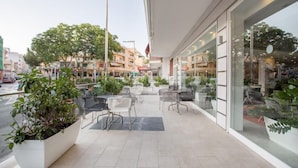 Un espacio al aire libre con mesas y sillas, plantas en macetas y vistas a la calle y edificios al fondo.