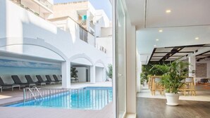 Una piscina interior con tumbonas, una terraza de madera y una zona de comedor con mesas y sillas.