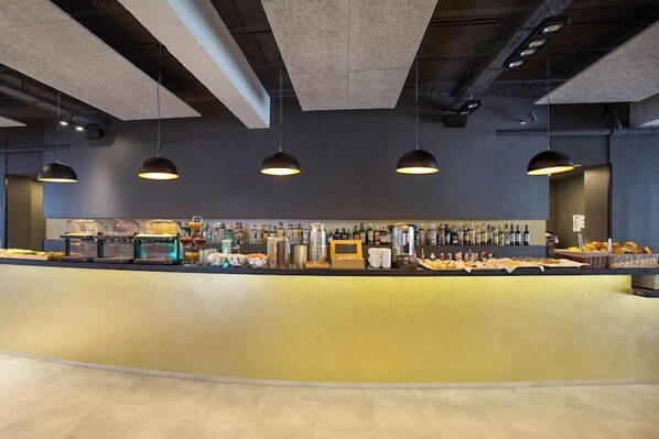 Zona de bar moderna con una barra curva, iluminación colgante y una variedad de bebidas y aperitivos.