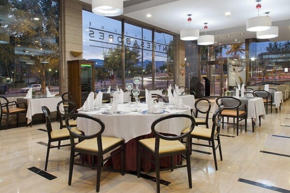 A restaurant with round tables set for dining, large windows, and modern lighting fixtures. - Elba Almeria Business & Convention Hotel (Almeria)