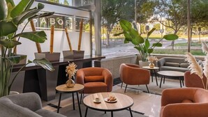A modern lounge area with comfortable seating, a reception desk, and large windows offering a view of the street. - Elba Almeria Business & Convention Hotel (Almeria)